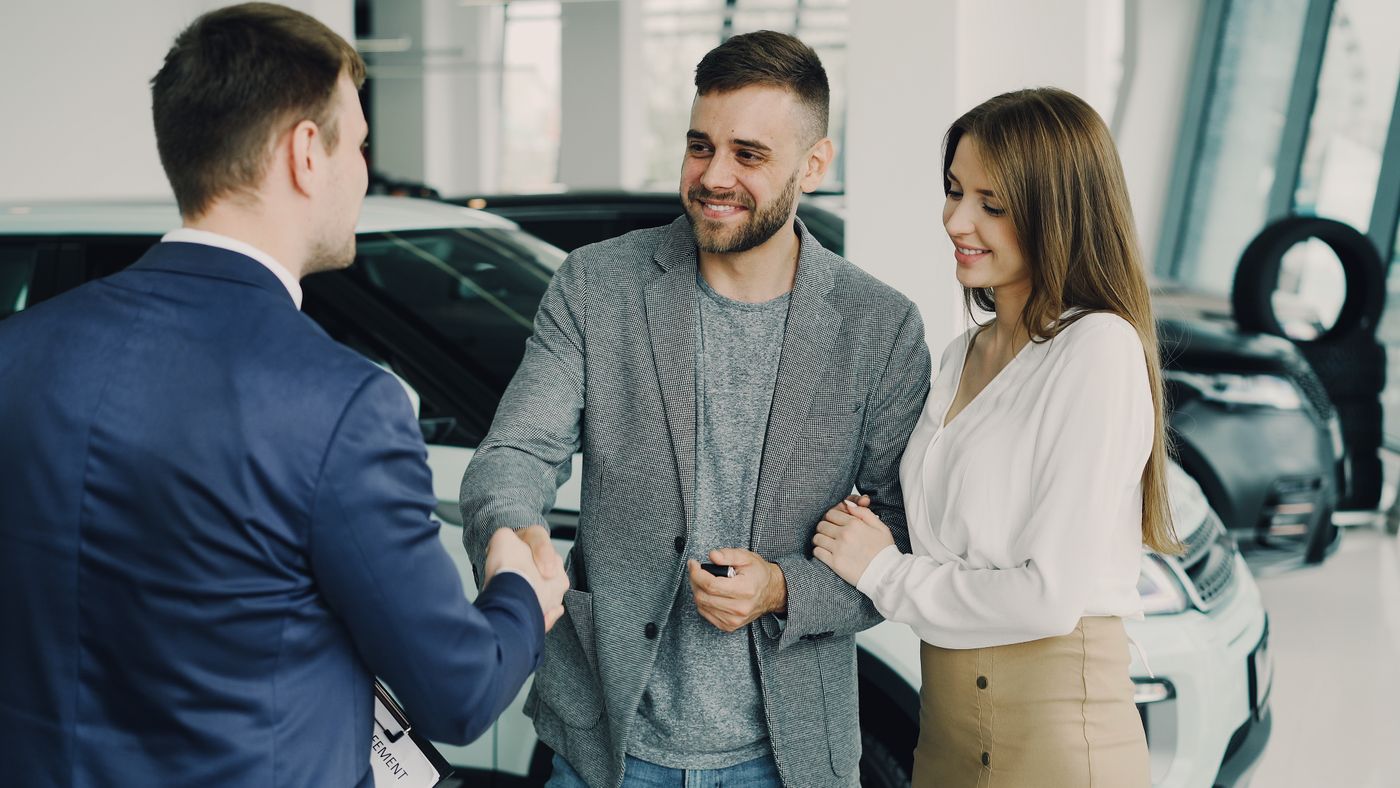 Smiling customers shaking hands after completing a vehicle deal